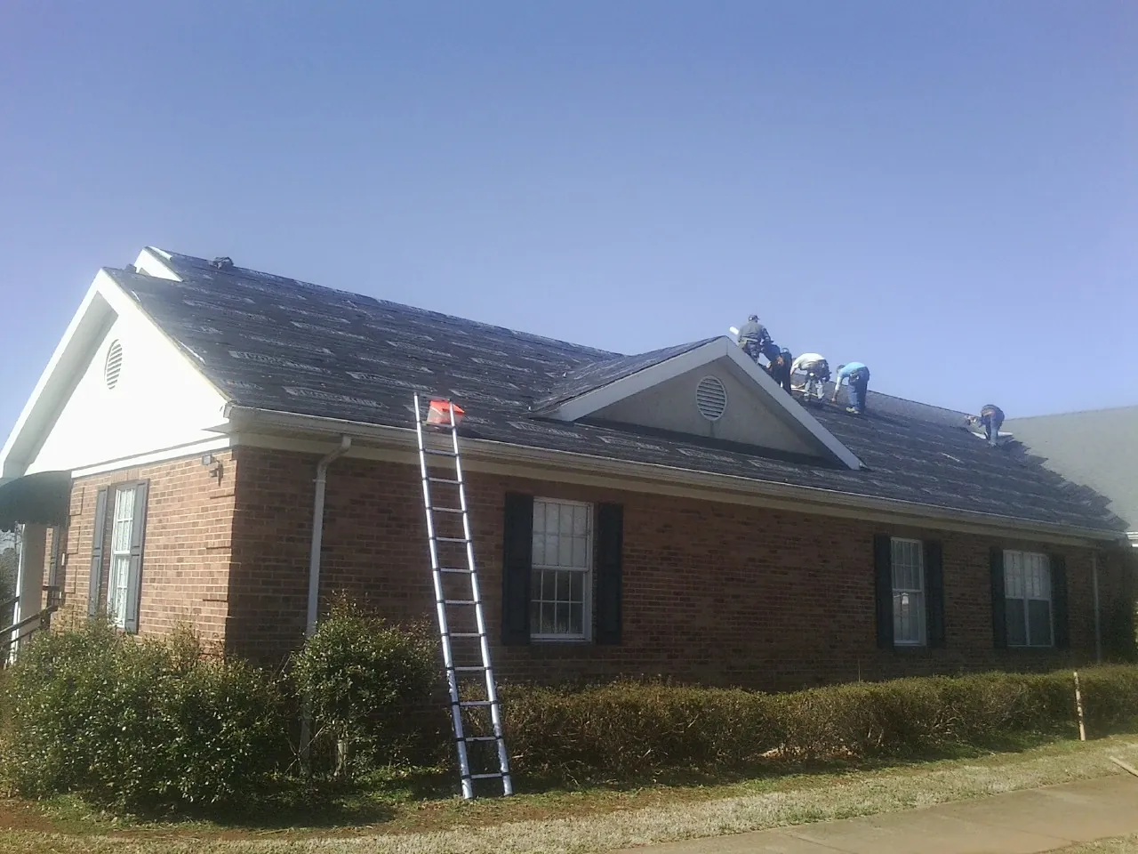 Crew tearing shingles off a brick ranch roof with a ladder set — Emergency Roof Repair work by our crew in Fall Creek