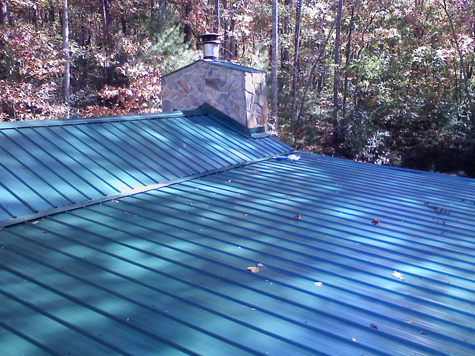 New green metal roof and stone chimney surrounded by autumn woods in Fall Creek