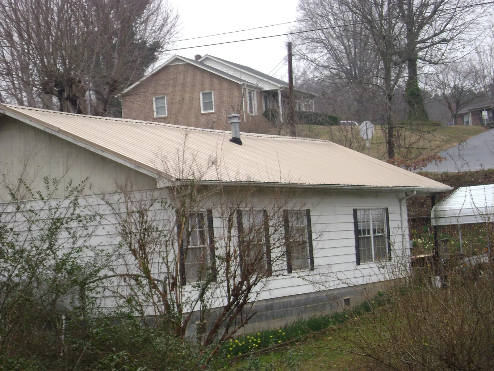 Tan metal roof on a white sided house set into a hillside — Commercial Roofing by Roofing Brothers in Fall Creek