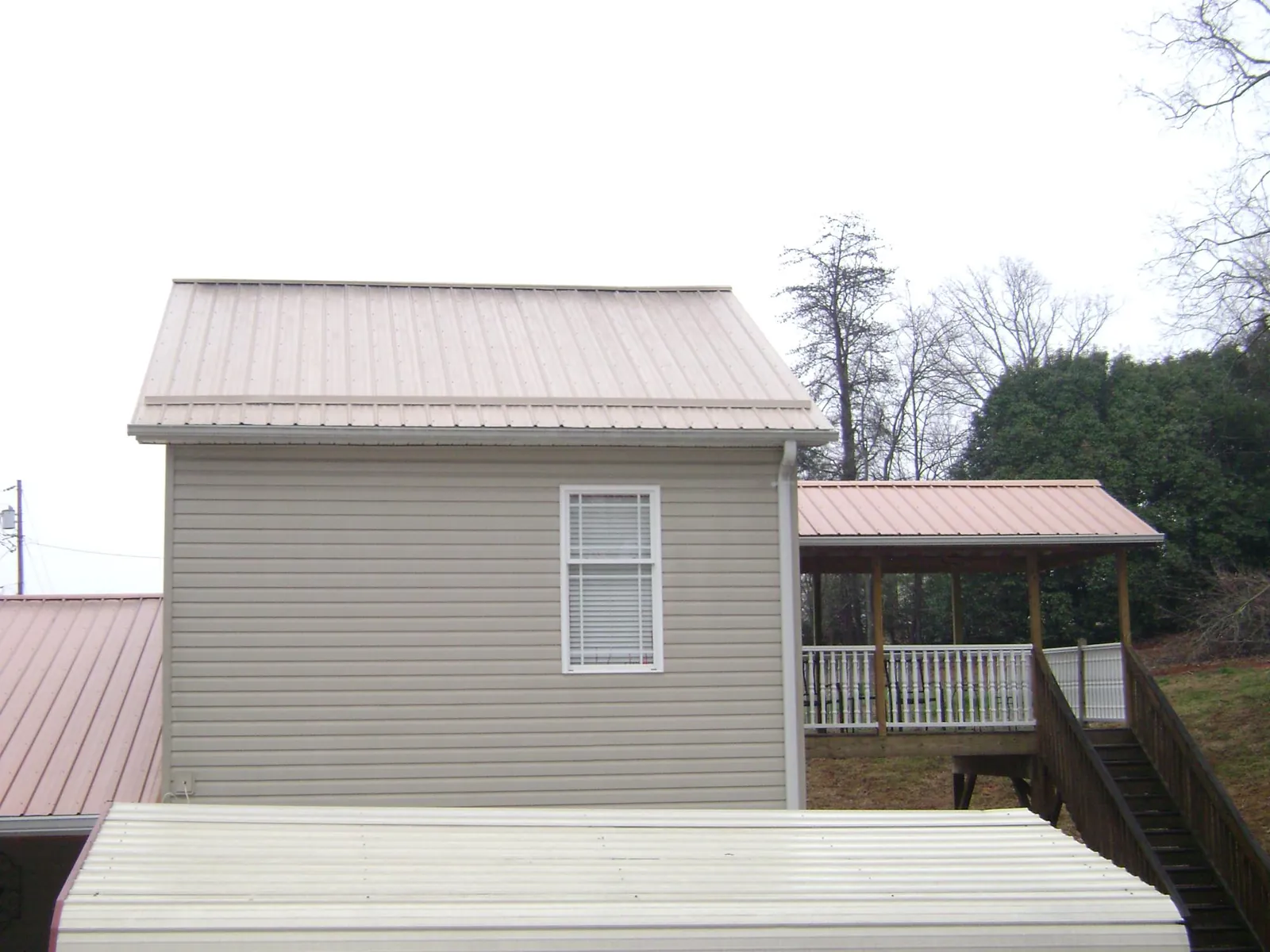 Tan metal roofs on a two story addition and attached porch, from a Roof Replacement job in Fall Creek